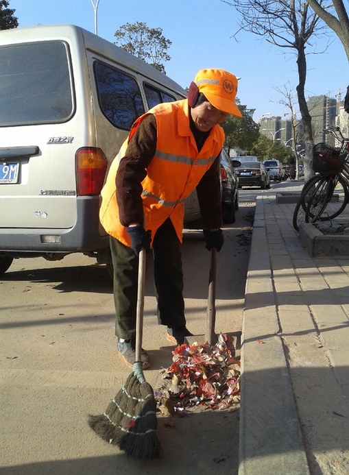 图为环卫工人在清理路面的烟花爆竹。